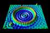 An image showing a ring of red, spike-like objects on a flat surface. Inside this ring there are some concentric ripples