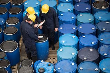 A photo of men in hard hats and overalls checking barrels of chemicals
